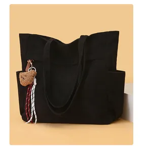 Dettaglio borsa tote in velluto a coste nero con ciondolo a orsetto e corda intrecciata