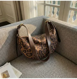 Detail of leopard print crescent bag with suede texture and brown leather strap on sofa