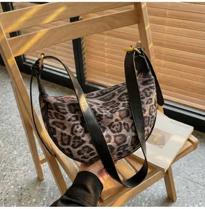Detail of leopard print suede half-moon bag with leather strap on a wooden chair