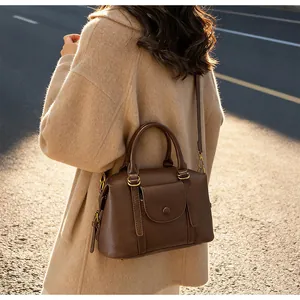 Detail of dark brown leather Boston bag showing round handles and crossbody strap texture