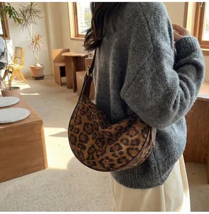 Side view of leopard print crescent bag worn as an underarm shoulder bag in a cozy setting
