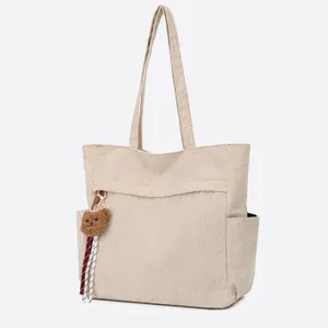 Dettaglio della borsa tote in velluto a coste beige con tasca frontale e ciondolo a orso