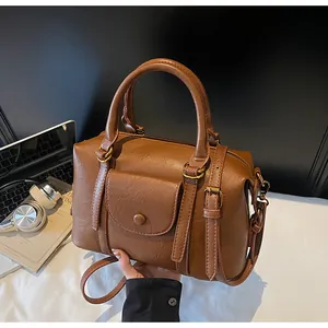 Detailed close-up of brown textured leather Boston bag with gold hardware and dual handles