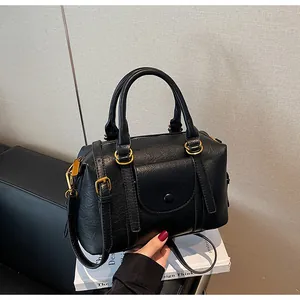 Close-up of black lychee texture Boston bag with gold hardware and a buckle front pocket