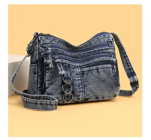 Detail of vintage blue washed denim crossbody bag with multiple zipper pockets and metal rings