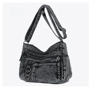 Detail view of washed black denim shoulder bag with multi-zipper pockets and metal buckle