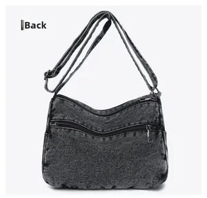 Detail view of the back side of a dark gray washed denim crossbody bag with zipper