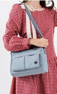 Detail of light blue nylon crossbody bag featuring double front flap pockets and grey strap