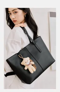 Detail of a large black leather tote bag with vertical stitching and a plush bear charm