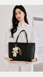 Detail of a black minimalist tote bag with a cute beige teddy bear plush charm attachment