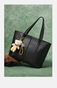 Detail of black PU leather tote bag with vertical stitching and brown plush bear charm