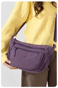 Detail einer dunkelvioletten Nylon-Umhängetasche mit Reißverschlüssen über einem gelben Pullover