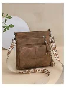 Detail of brown canvas crossbody bag with tassel and ethnic embroidered strap