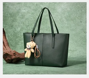 Detail of dark green tote bag with vertical stitching and plush bear charm on wood
