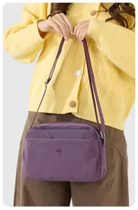 Detail einer lila Nylon-Umhängetasche mit mehrlagigen Reißverschlüssen auf gelber Jacke