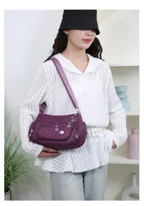 Detail view of purple quilted nylon crossbody bag featuring multiple zipper pockets on model
