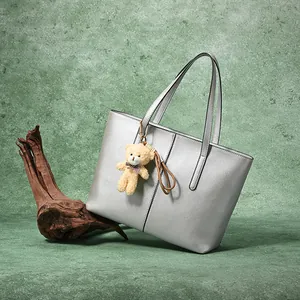 Minimalist silver metallic leather tote bag with a cute plush bear pendant on green background