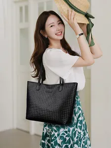 Close-up of black woven leather tote bag featuring a rectangular sport logo and dual straps