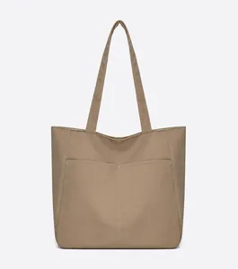 Front detail of khaki canvas tote bag featuring dual front pockets and white stitching