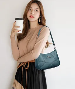 Detail of teal leather shoulder bag with stitching and kangaroo emblem on autumn model