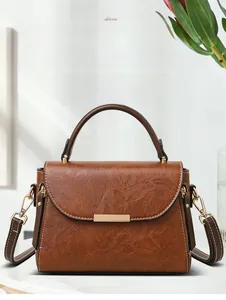 Detail of a brown textured crossbody bag with a gold buckle and removable shoulder strap