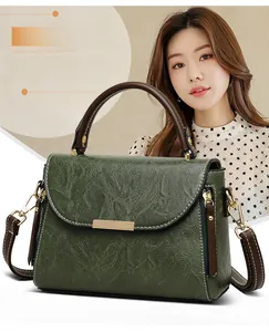 Detail of dark green vintage textured handbag with brown handle and gold hardware