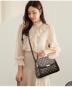 Close-up of a brown checkered handbag with gold hardware worn by a model in a blouse