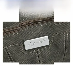 Macro view of metallic silver logo plate on durable charcoal gray crossbody bag fabric