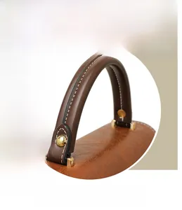 Close-up of brown leather handbag handle with white stitching and gold metal hardware