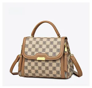 Detail view of brown checkerboard handbag with leather handle and golden metal hardware