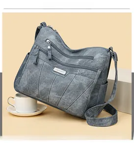 Detailed view of gray canvas crossbody bag with multiple zipper compartments and metal logo