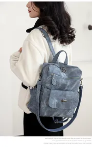 Detail of grey-blue leather backpack showing adjustable straps and multiple zipper pockets