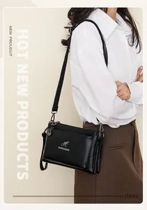 Detalle de bolso bandolera de cuero negro con varios compartimentos con cremallera y logo metálico
