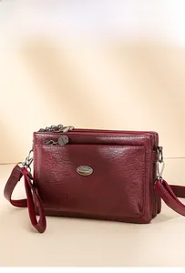 Close-up of wine red faux leather crossbody bag with three zipper compartments