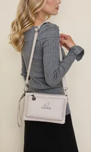 Detalle de bolso bandolera beige de piel suave con logo de canguro y correa ajustable
