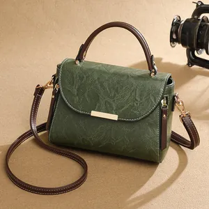 Retro green leather crossbody bag with brown handle and gold buckle on a warm background