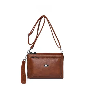 Brown faux leather crossbody bag detail featuring triple zipper pockets and a metal logo