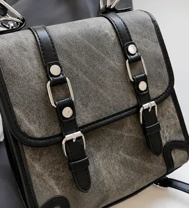 Detail of grey canvas shoulder bag featuring black leather straps and silver metal buckles