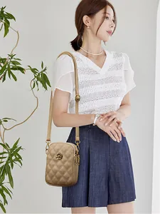 Détail d'un sac téléphone en cuir doré matelassé avec une boucle en fleur de camélia