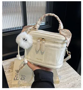Detail view of cream box bag with silk scarf handle and plush monster charm accessory
