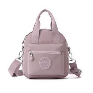 Vista frontal de un bolso bandolera de nailon rosa empolvado con asas dobles y cremalleras