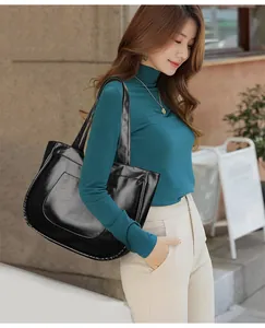 Side view of large black leather tote bag with wide strap on model in city street
