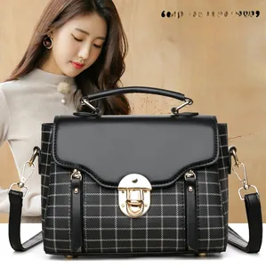 Detail of black crossbody bag with white stitched grid and golden metal turn-lock closure