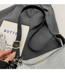 Close-up of silver dumpling bag featuring houndstooth texture and black adjustable strap