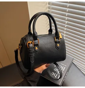 Detalle de bolso Boston negro con piel texturizada, asas dobles y herrajes dorados vintage