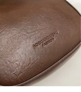 Detailansicht der Litchi-Maserung und des geprägten Logos auf der dunkelbraunen Ledertasche