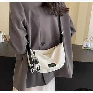 Detail of cream crescent bag with adjustable black strap and checkerboard charm
