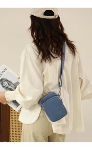 Blue nylon crossbody phone bag shown from a side view on a model in a minimalist setting
