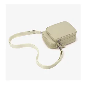 Detail of sage green nylon crossbody bag showing three zipper compartments and wide strap
