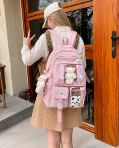 Mochila escolar rosa con diseño multibolsillo y amuleto de oso mostrada en modelo
